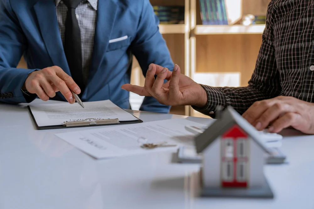 Close-up of hands signing a document next to a small house model