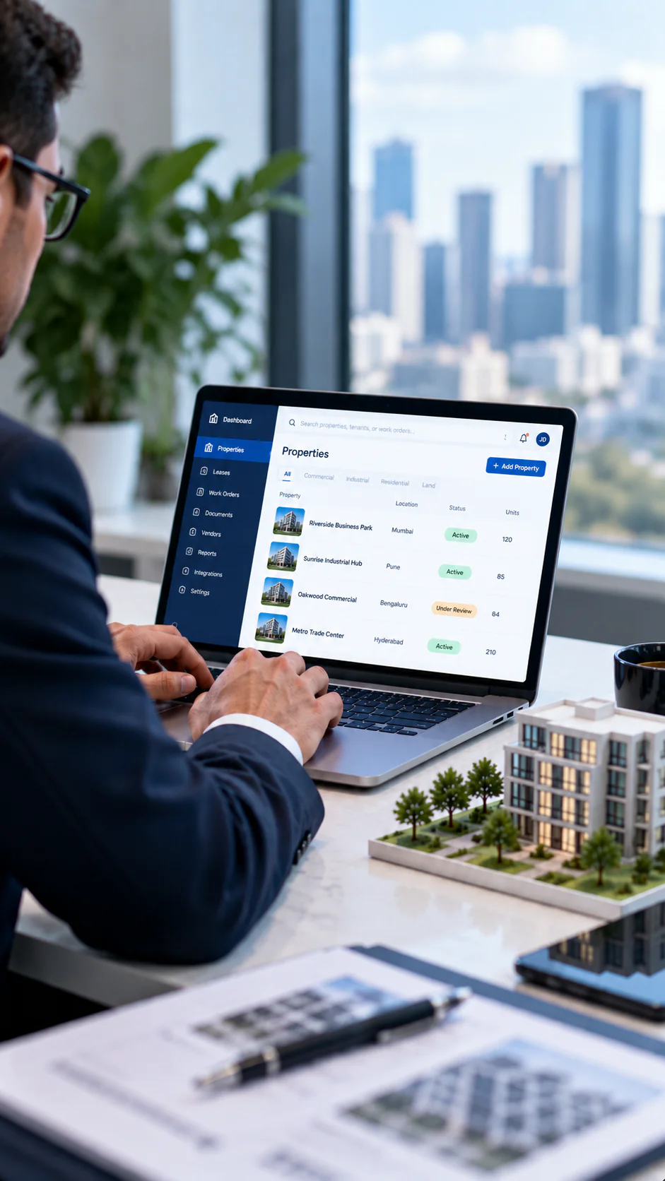 A person works at a laptop showing a workflow dashboard, with a building model on the desk